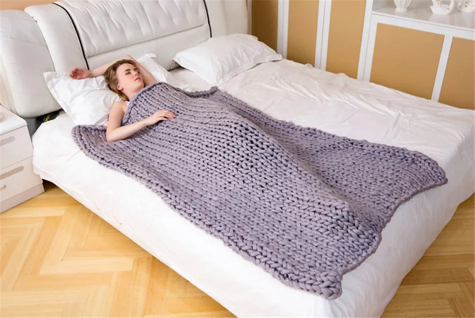 A woman sleeps on a bed under a large, grey, chunky knit yarn blanket.