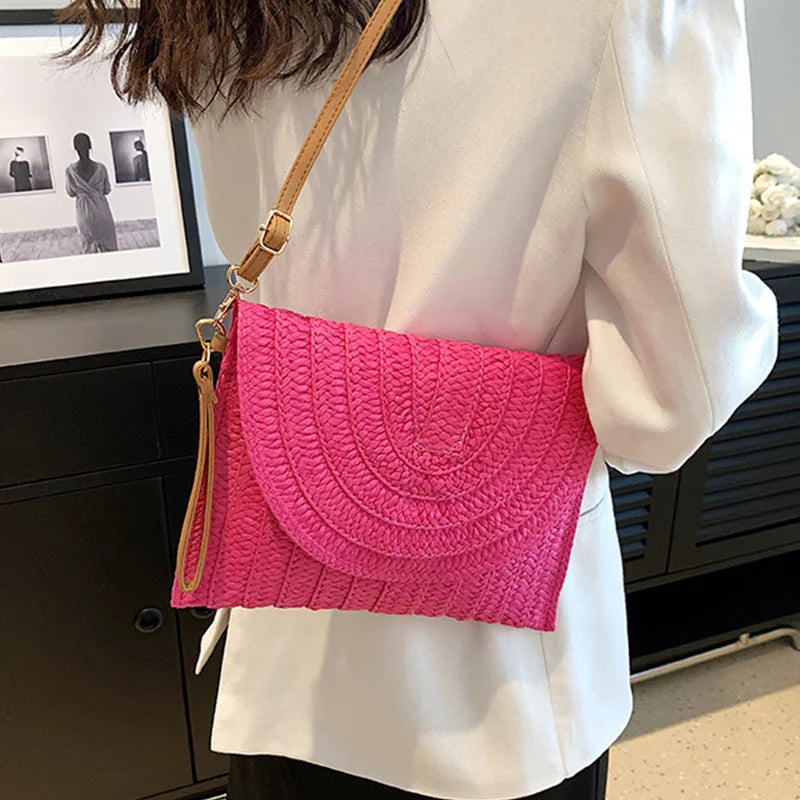 Bright pink woven straw envelope crossbody bag with an adjustable strap, ideal for a beach vacation.
