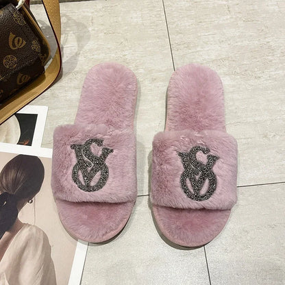 Light pink fuzzy slip-on shoes with rhinestone logos and a non-slip sole for comfortable home lounging.