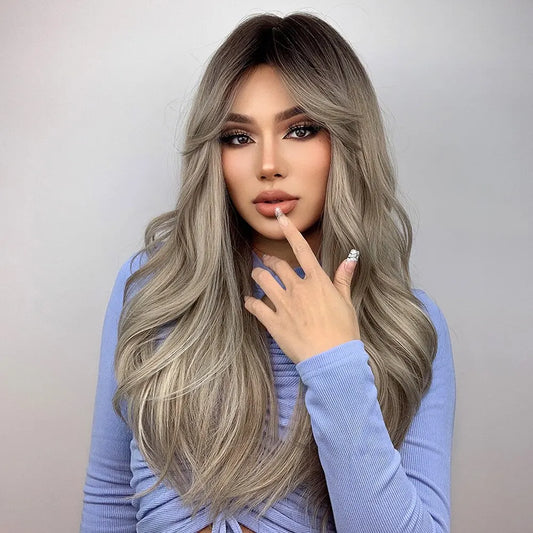 Long ombre wig with dark roots, face-framing bangs, and soft waves worn with a periwinkle top.