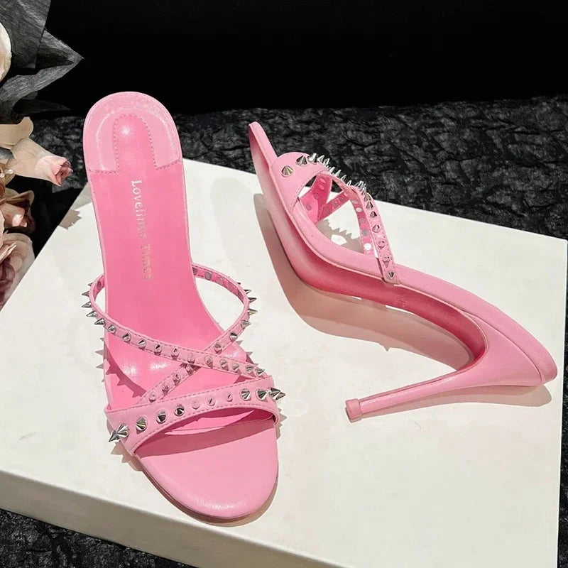 Pink open toe sandals with silver rivets and slim heels, a strappy design for evening wear.