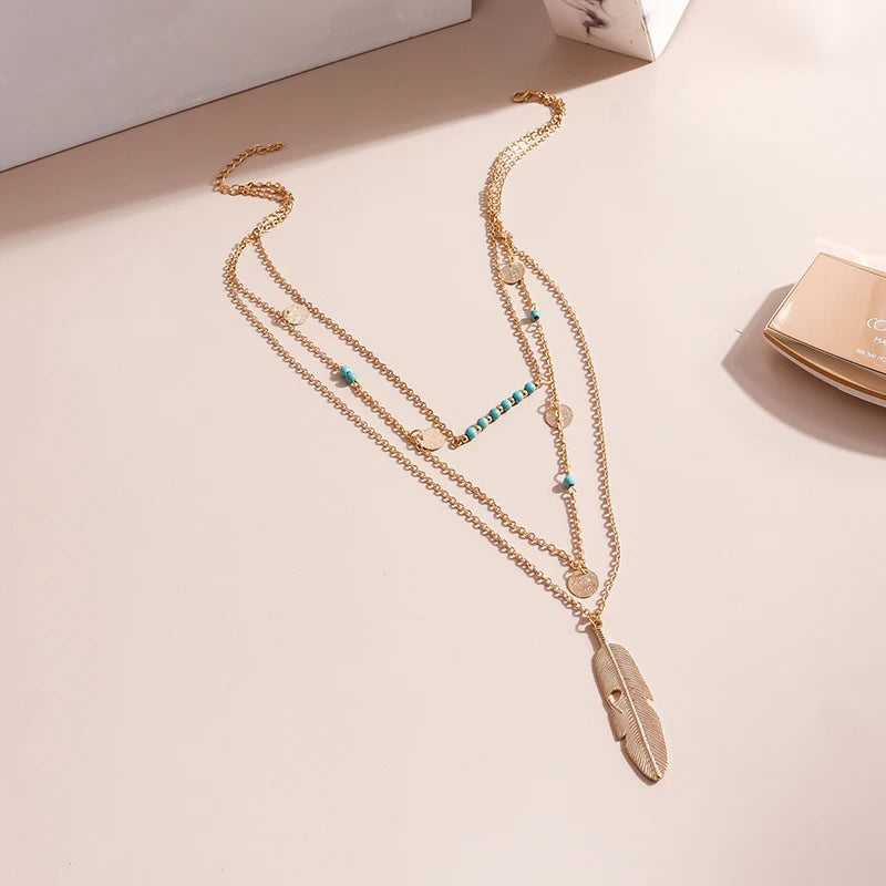 Multi-strand gold metal necklace with turquoise beads, coin charms, and a feather pendant.