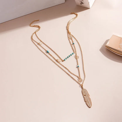 Multi-strand gold metal necklace with turquoise beads, coin charms, and a feather pendant.