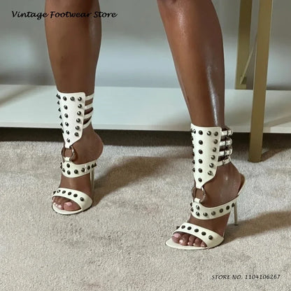 White strappy stiletto heels with silver metal rivets, buckle closures, and an open toe design for formal events.