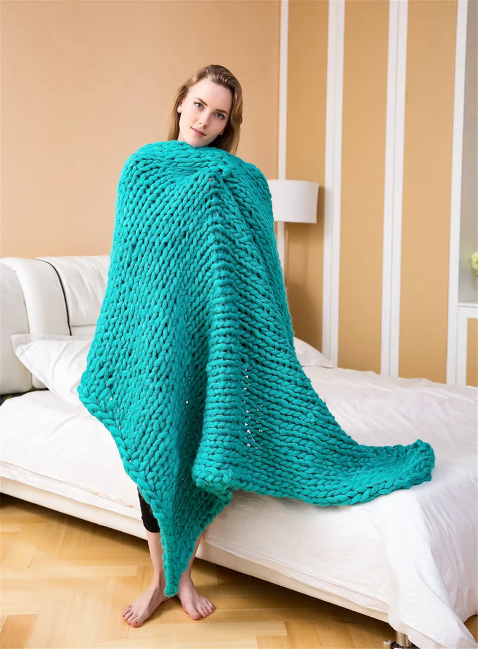 A woman wrapped in a chunky, turquoise hand-knitted yarn blanket.