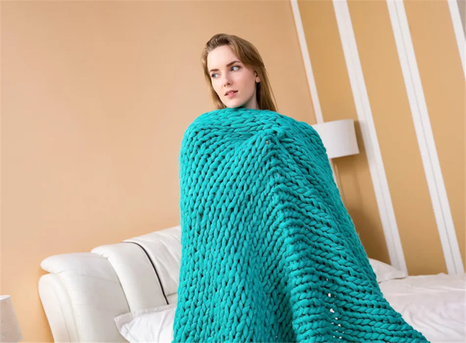 Teal chunky hand-knit yarn blanket wrapped around a woman sitting on a white sofa.