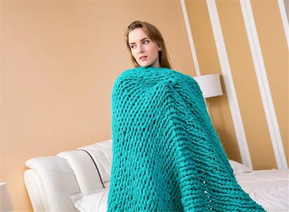 Teal chunky hand-knit yarn blanket wrapped around a woman sitting on a white sofa.