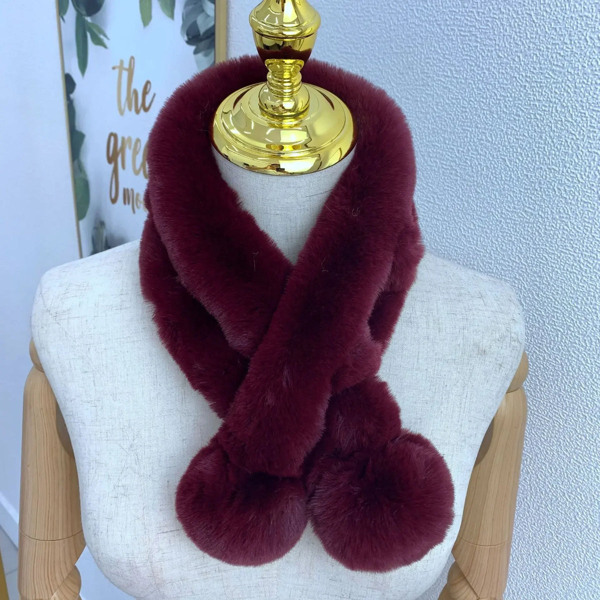 Burgundy plush faux fur cross scarf with two large pom-pom ends wrapped around a mannequin.