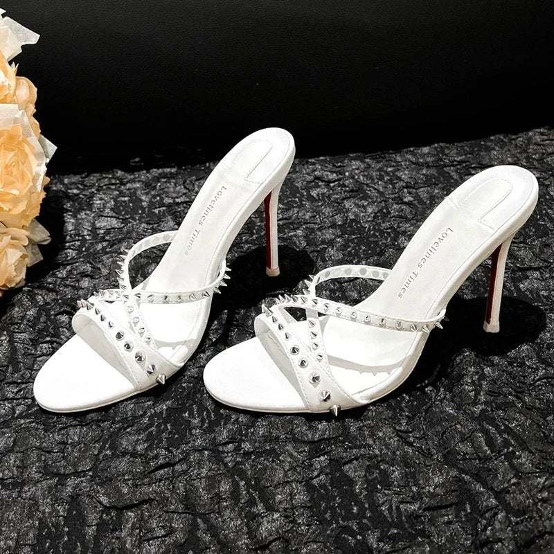 White open toe sandals with silver rivets and slim heels, a strappy design for evening wear.