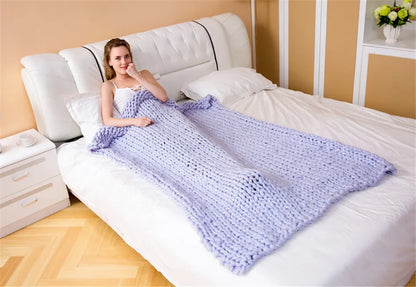 Grey chunky hand-knitted yarn roving blanket draped over a woman lying on a white bed.
