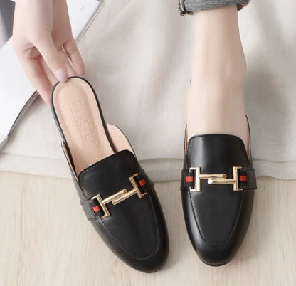 Black leather slip-on mules with a gold metal chain detail and red stripe for casual outdoor wear.