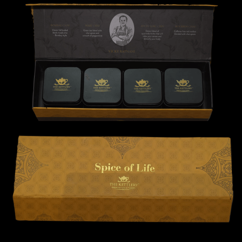 Open tea gift box showing four black metal tins with gold teapot logos, with closed box below.