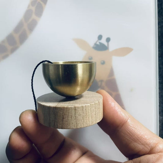 Small brass singing bowl resting on a round wooden base, held by a hand.