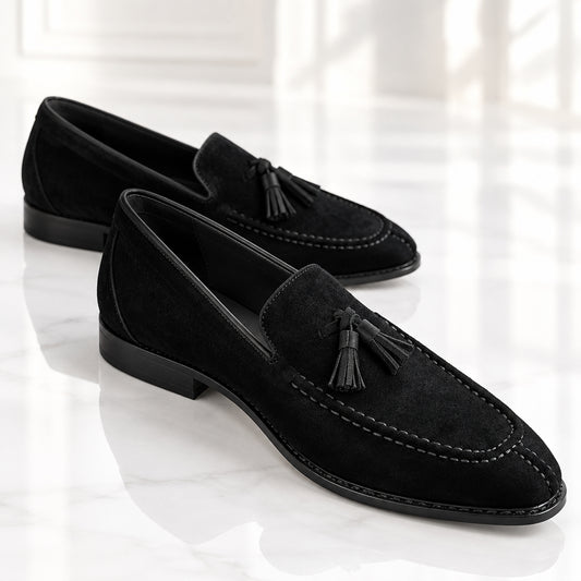 Black suede tassel loafers for men on a white surface with visible stitching.