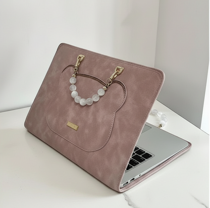 Dusty pink suede laptop case with white beaded handle and gold hardware on white surface.