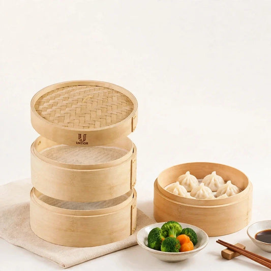Stacked bamboo tiered steamer baskets with lid beside a basket filled with dumplings, broccoli, and dipping sauce.