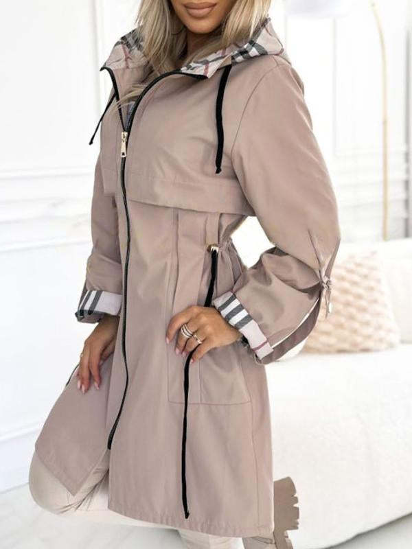 Woman wearing a beige hooded coat with black drawstrings, zipper, and plaid lining on the hood and cuffs.