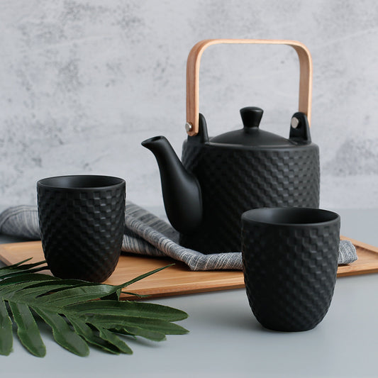 black basketweave ceramic teapot with wooden handle and two matching cups on wooden tray