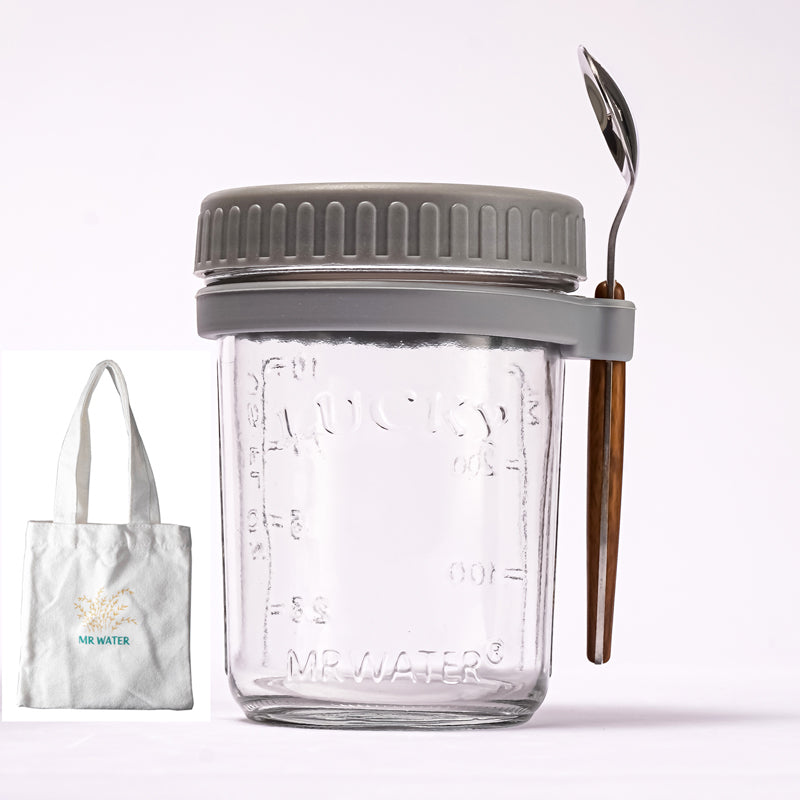 Clear glass overnight oats jar with grey lid and spoon holder, spoon, and a small tote bag