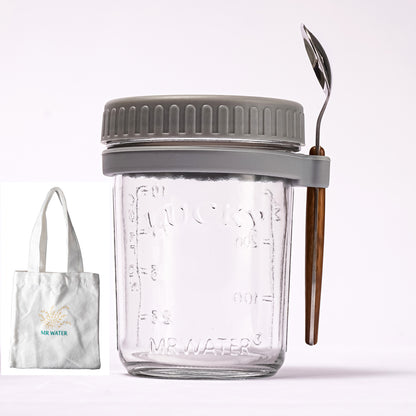 Clear glass overnight oats jar with grey lid and spoon holder, spoon, and a small tote bag