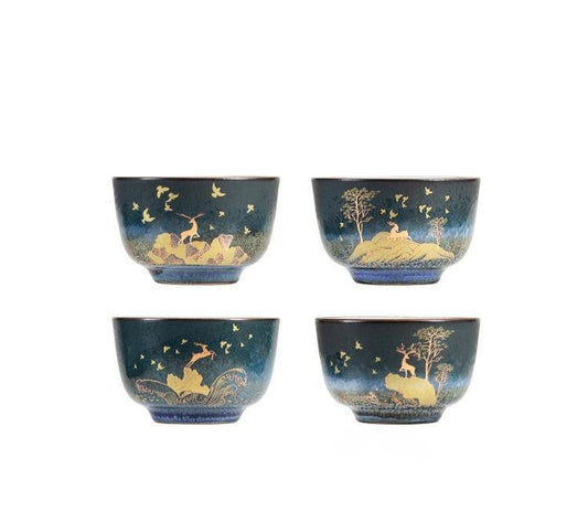 Four dark blue ceramic teacups featuring gold foil landscapes with deer and birds.