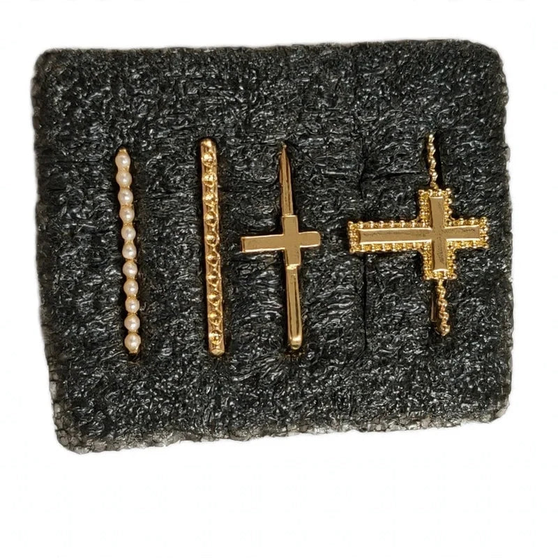 Four gold smartwatch band charms on dark foam, including a pearl bar, textured bar, and two cross designs.