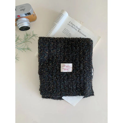 Dark textured knit scarf with a small label on a surface with a camera and book.