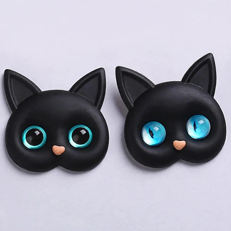 Two black cat head phone grips with large blue eyes on a light surface.
