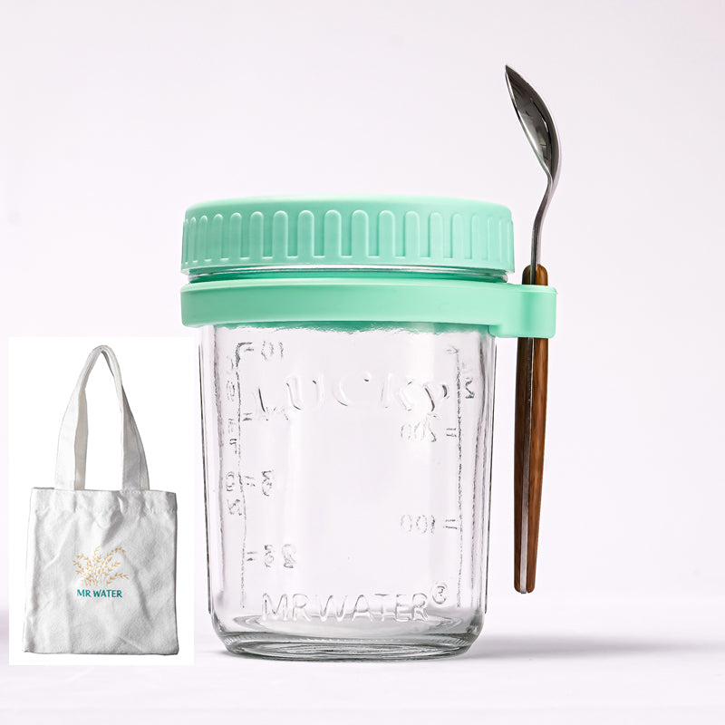 Clear glass oat jar with a mint green lid, spoon holder, metal spoon, and a small white tote bag.