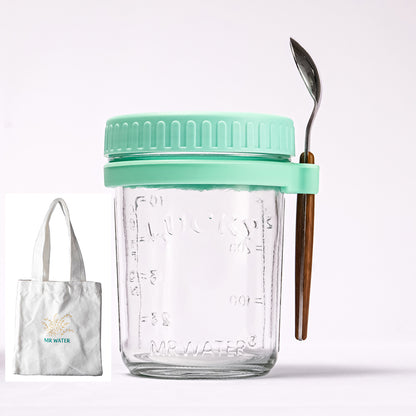 Clear glass oat jar with a mint green lid, spoon holder, metal spoon, and a small white tote bag.