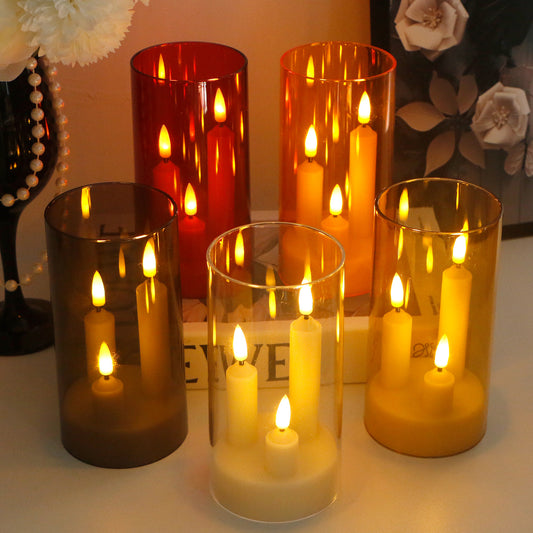 Five tall glass cylinder holders containing lighted LED pillar candles in various warm tones on a surface.