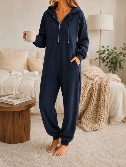 Model in a hooded zip-up jumpsuit with half-zip front, hand resting in the side pocket