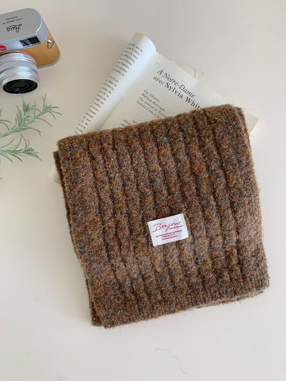 Folded brown textured knitted scarf with small label beside vintage camera and book.