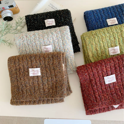 Six folded chunky knit winter scarves in various colors displayed on a white surface with props.