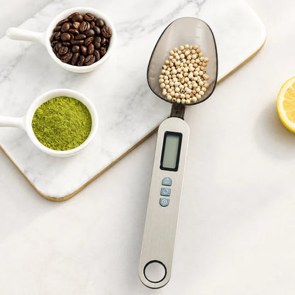 Digital measuring spoon scale with white peppercorns in the scoop, on a marble board with coffee beans and matcha powder.