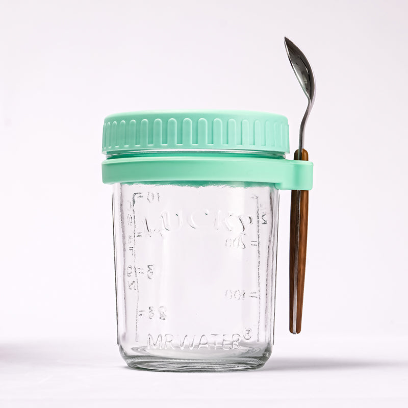 Clear glass jar with light green lid and matching silicone spoon holder securing a spoon with a wooden handle.