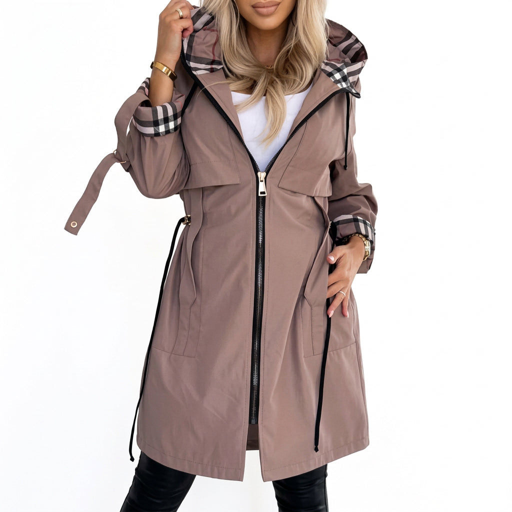 Woman wearing a beige hooded coat with black, white, and red plaid lining on the hood and rolled cuffs.