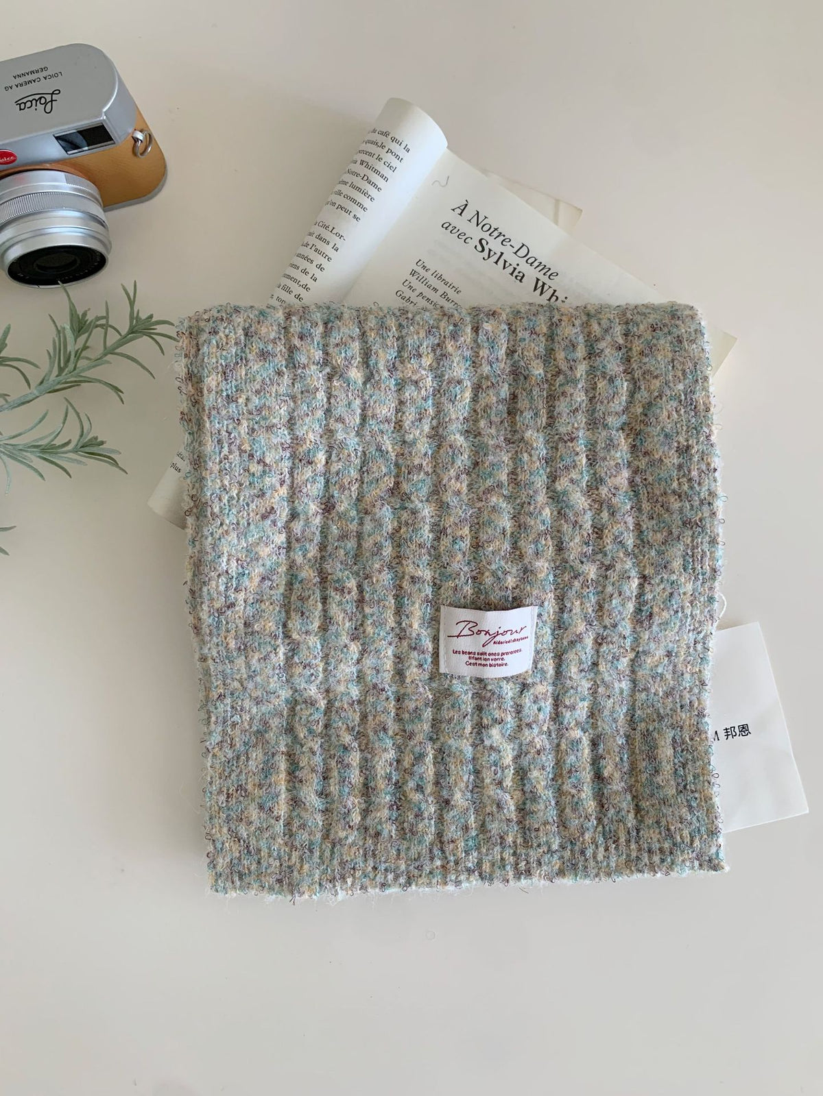 Folded multicolored textured winter knit scarf with a small white label reading Bonjour
