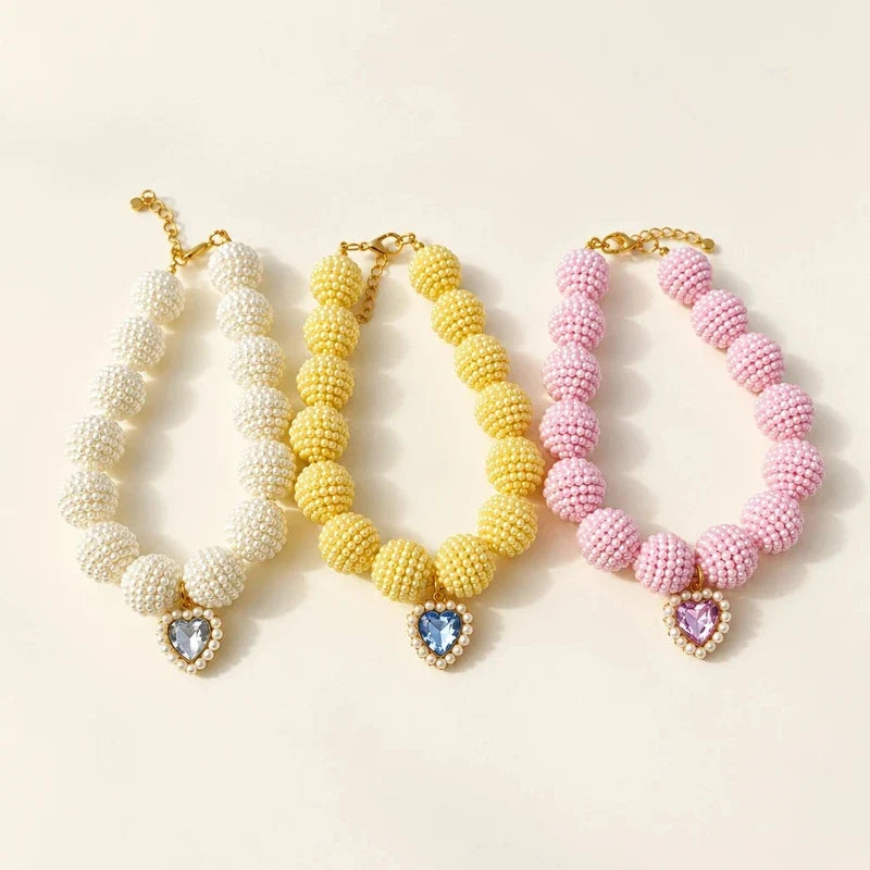 Three beaded pet necklaces in white, yellow, and pink, each featuring a heart crystal pendant.