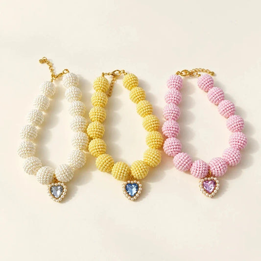 Three beaded pet necklaces in white, yellow, and pink, each featuring a heart crystal pendant.