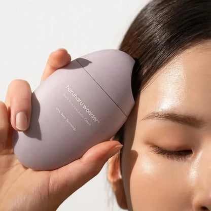 A person holding an oval purple moisturizer container near their temple.