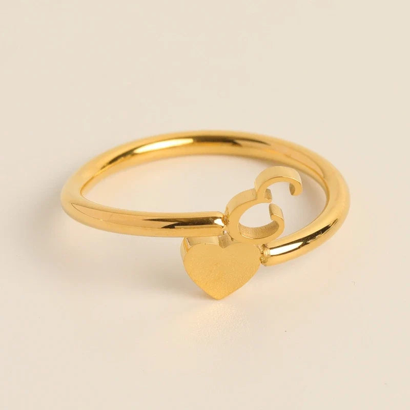 Gold adjustable ring featuring a dangling heart charm and initial letter E.
