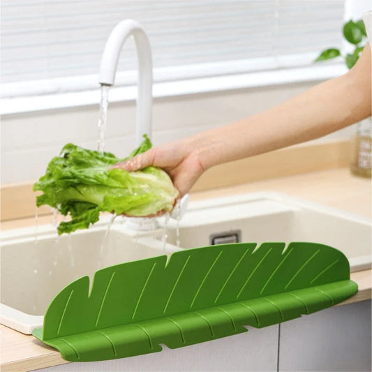 Green leaf-shaped silicone sink splash guard attached to a kitchen sink counter while water runs from the faucet