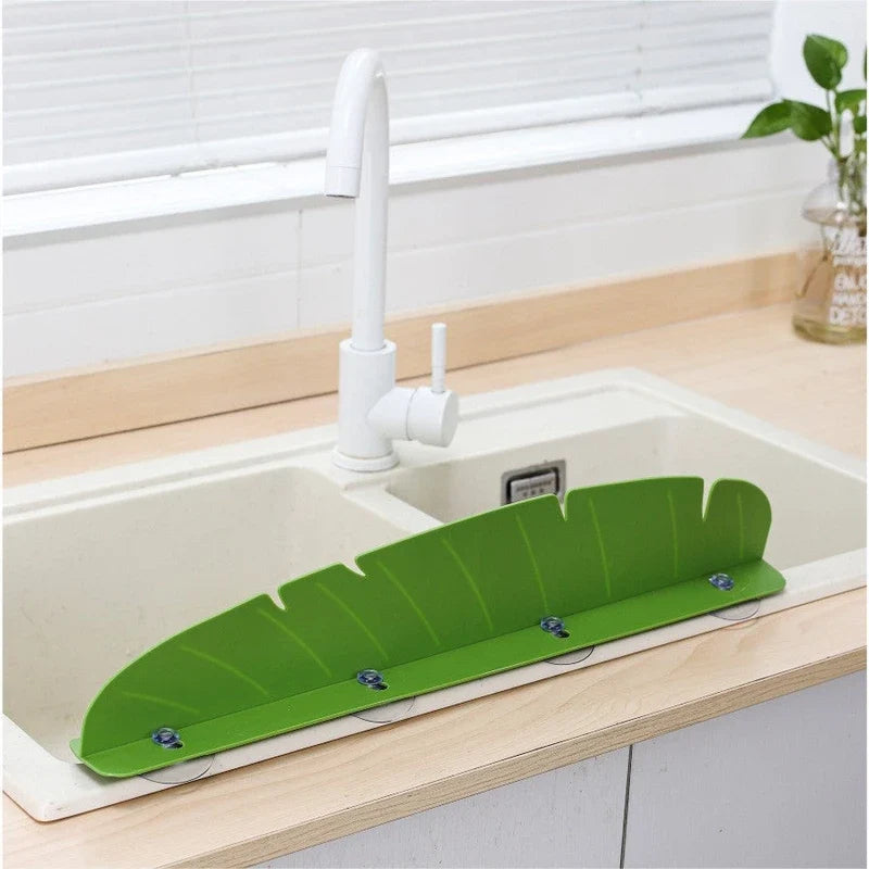 Green leaf-shaped sink splash guard mounted with suction cups on a kitchen sink.