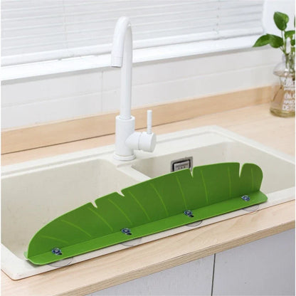 Green leaf-shaped sink splash guard mounted with suction cups on a kitchen sink.