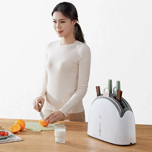 A woman slicing an orange next to a white and grey knife sterilizer dock on a wooden table.