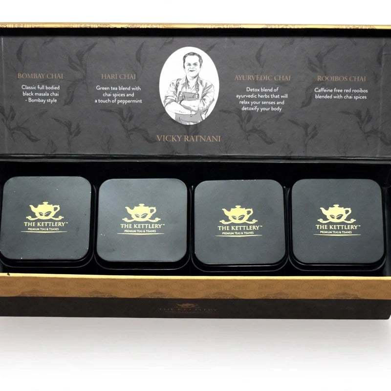 Opened tea gift box displaying four black square tins with gold teapot logos and text descriptions inside the lid.