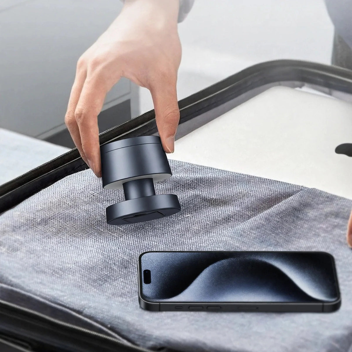 A hand holding a compact dark gray wireless charging dock near a smartphone inside a suitcase.