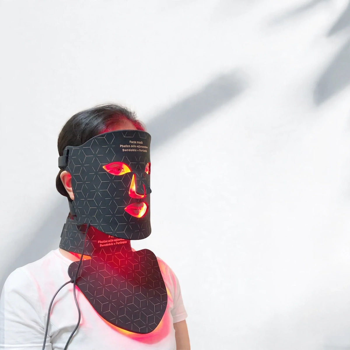 Person wearing a black LED silicone facial and neck mask emitting red light, with overlaid benefit icons.