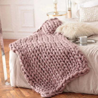 Dusty pink chunky knit throw blanket draped across a bed with pillows